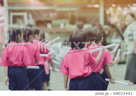 Back view of little girls use paper rolls instead of long cheerleader Baton Sticks for school parade marching practice. 68023401