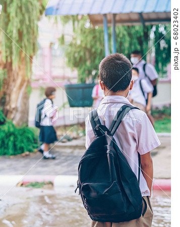 Male elementary school student wear face mask to prevent the Coronavirus(Covid-19) wait for her parents to pick her up to return home after school and the rain just stop in front of the school gate 68023402