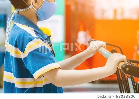 A boy wearing face mask to prevent the spread of the Corona Virus (Covid-19) shopping in a supermarket. Boy with shopping cart during virus outbreak in grocery store. New normal lifestyle. A boy wearing face mask to prevent the spread of the Corona Virus (Covid-19) shopping in a supermarket. Boy with shopping cart during virus outbreak in grocery store. New normal lifestyle. 68023806