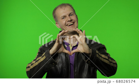 Brutal rocker man taking out heart gesture from his jacket and demonstrating romantic emotions 68026574