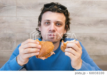 Man eating a hotdog and shawarma simultaneously sitting in cafe. Man eating a hotdog and shawarma simultaneously sitting in cafe. 68038100