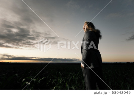 young stylish guy stands in a field in a gray suit at sunset. Blond with long hair in a cornfield 68042049