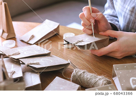 Woman makes christmas advent calendar for kids. Writes a number on the bag by brush and white paint. Close-up hands. Woman makes christmas advent calendar for kids. Writes a number on the bag by brush and white paint. Close-up hands. 68043366