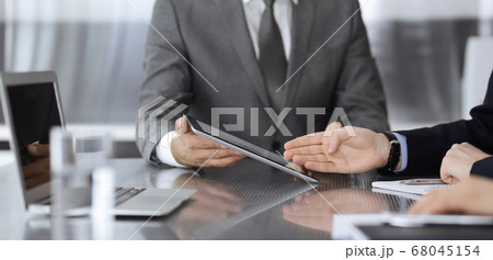 Unknown businessman using tablet computer and working together with his colleague while sits at the glass desk in modern office. Teamwork and partnership concept Unknown businessman using tablet computer and working together with his colleague while sits at the glass desk in modern office. Teamwork and partnership concept 68045154