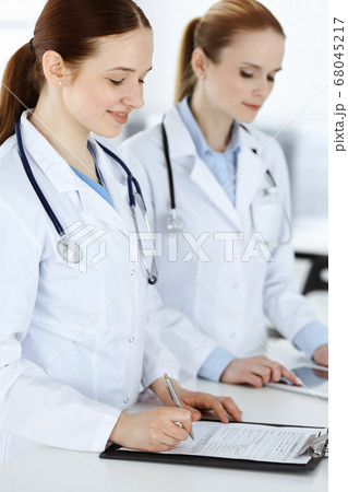 Woman-doctor at work. Female physician or internal student filling up medical documents or prescription while standing in clinic reception desk. Data in medicine 68045217
