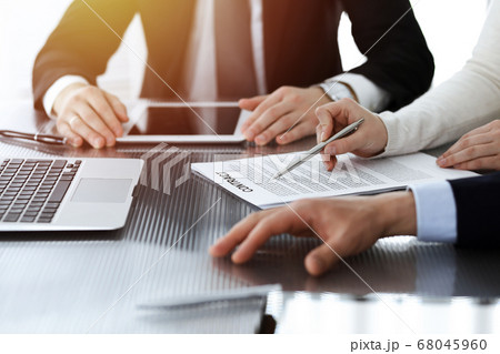 Business people discussing contract while working together in sunny modern office. Unknown businessman and woman with colleagues or lawyers at meeting 68045960