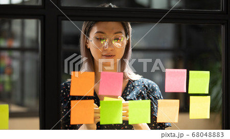 Focused asian coach working on project writing on sticky notes 68048883