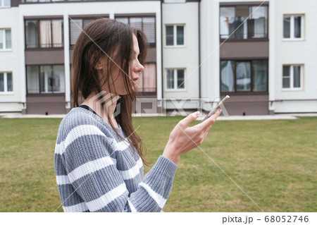 Beautiful brunette woman reading a message on mobile phone walking near the home. Beautiful brunette woman reading a message on mobile phone walking near the home. 68052746