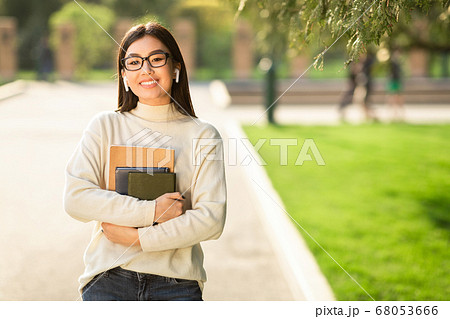Girl in glasses and headphones standing in park Girl in glasses and headphones standing in park 68053666