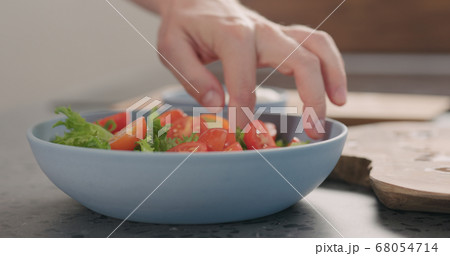 making salad with frisee lettuce, tomatoes amd mozzarella in a blue bowl on kitchen countertop 68054714