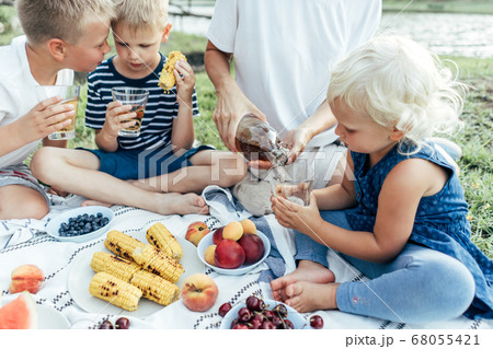 A family sits on the tablecloth and eats fruits and berries. A family sits on the tablecloth and eats fruits and berries. 68055421