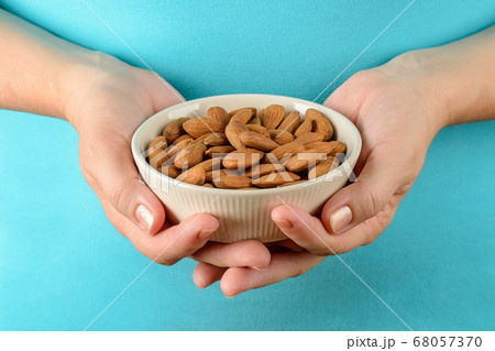 Caucasian woman hands hold beige ceramic bowl with raw almonds. Caucasian woman hands hold beige ceramic bowl with raw almonds. 68057370