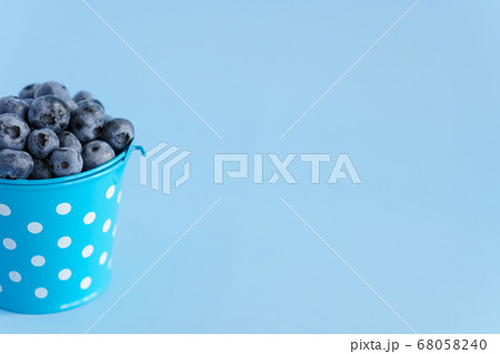 fruits and vegetables, vitamin, healthy food and drink, traditional medicine, gastronomy concept - layout purple blueberry berries in blue bucket with white dots on bright blue background copy space fruits and vegetables, vitamin, healthy food and drink, traditional medicine, gastronomy concept - layout purple blueberry berries in blue bucket with white dots on bright blue background copy space 68058240