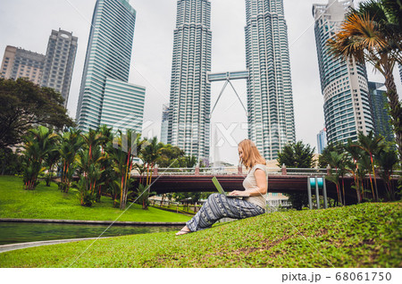 A young woman in casual dress using laptop in a tropical park on the background of skyscrapers. Mobile Office concept 68061750