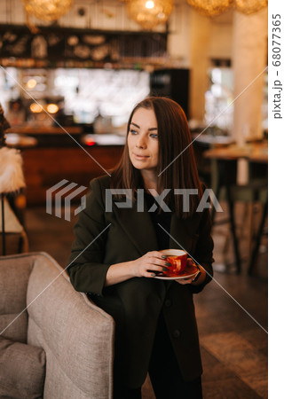 Close up of face of young woman holding cup of tasty hot coffee in hand while standing in restaurant Close up of face of young woman holding cup of tasty hot coffee in hand while standing in restaurant 68077365