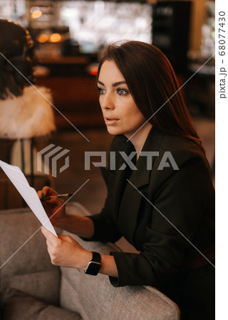 Portrait of beautiful young woman wearing stylish clothes in restaurant holding paper documents. 68077430
