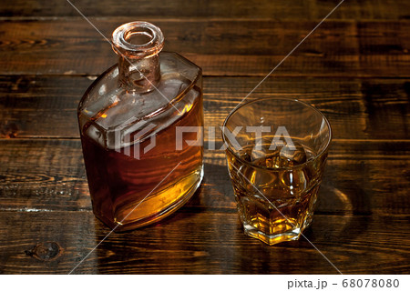 A glass of alcohol near a bottle. Old whiskey bottle on black wooden table. Drinks on a dark blurred background. A glass of alcohol near a bottle. Old whiskey bottle on black wooden table. Drinks on a dark blurred background. 68078080