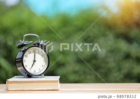 Vintage alarm clock with white book on wooden desk with green nature background Vintage alarm clock with white book on wooden desk with green nature background 68078312