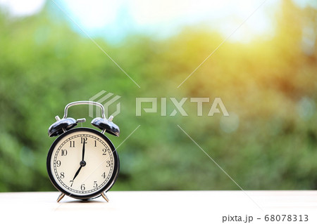 Vintage alarm clock on wooden desk with green nature and sunlight background Vintage alarm clock on wooden desk with green nature and sunlight background 68078313