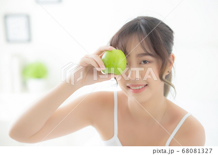 Beautiful portrait young asian woman holding and eating green apple fruit in the bedroom at home. 68081327