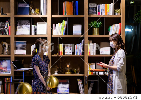 オフィスの本棚の前でミーティングするソーシャルディスタンスをとったマスクのビジネスウーマン 68082571
