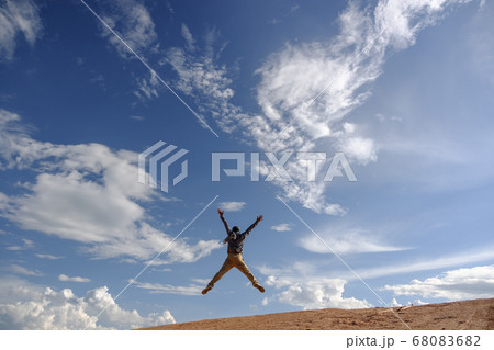 Man jump and stretching out his arms on grounds.Asian men wear gray shirts, brown pants are standing outdoors.Look at the copy space.Wear a hat and scarf. Man jump and stretching out his arms on grounds.Asian men wear gray shirts, brown pants are standing outdoors.Look at the copy space.Wear a hat and scarf. 68083682