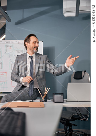 Handsome man sitting on table in office Handsome man sitting on table in office 68084842