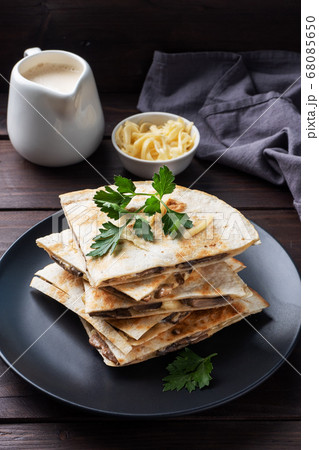 Pieces of quesadilla with mushrooms sour cream and cheese on a plate with parsley leaves. Wooden background copy space. Pieces of quesadilla with mushrooms sour cream and cheese on a plate with parsley leaves. Wooden background copy space. 68085650