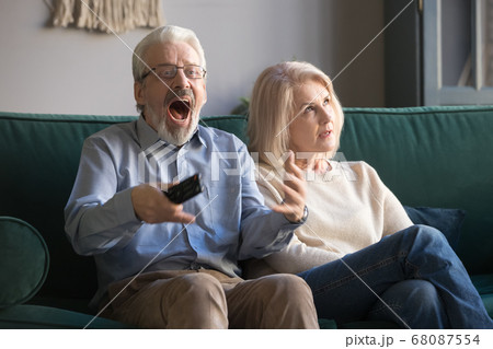 Bored middle-aged wife annoyed with senior husband watching sport tv 68087554