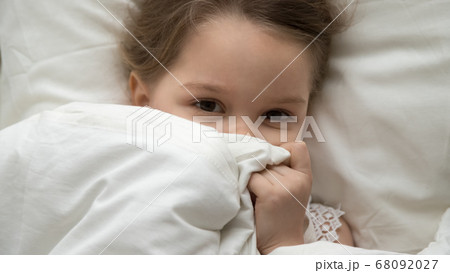 Cute kid girl looking at camera under blanket in bed Cute kid girl looking at camera under blanket in bed 68092027