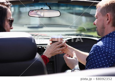 Man and woman sit in car and hold glass of drink together Man and woman sit in car and hold glass of drink together 68092352