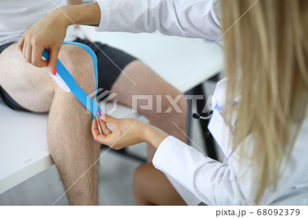 Nurse should glue kinesio tape on athlete's injured knee Nurse should glue kinesio tape on athlete's injured knee 68092379