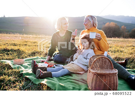 Small girl with mother and grandmother having picnic in nature at sunset. 68095522