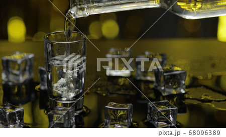Barman pour frozen vodka from bottle into shot glass. Ice cubes against shiny gold party background 68096389