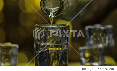 Barman pour frozen vodka from bottle into shot glass against shiny gold party celebration background 68096390
