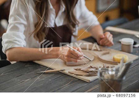 Craftsman hands connect the clay parts made of raw clay, master fingers work with pieces of clay, female sits at a workshop behind the table 68097156