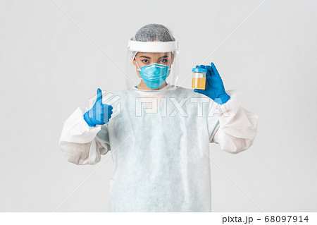 Covid-19, coronavirus disease, healthcare workers concept. Side view of serious-looking tech lab employee, researcher in personal protective equipment examine urine analyzes, show thumbs-up 68097914