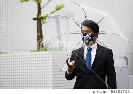 雨のが降る中ビニール傘をさしマスクをして通勤するミドルビジネスマン  雨のが降る中ビニール傘をさしマスクをして通勤するミドルビジネスマン  68102735