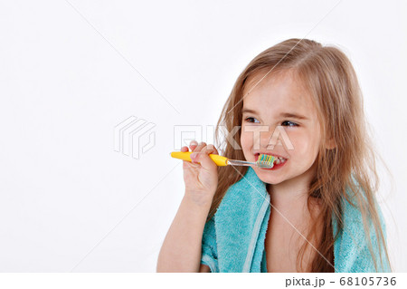 a little girl brushes her teeth on a white background. portrait of a child with a yellow toothbrush. blue towel around her neck. morning hygiene procedures a little girl brushes her teeth on a white background. portrait of a child with a yellow toothbrush. blue towel around her neck. morning hygiene procedures 68105736
