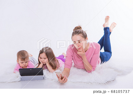 Modern technologies in everyday life: woman talks on phone through headset, children watch cartoon on tablet. Hobbies and recreation with gadgets. Family vacation. Parents with girls on floor Modern technologies in everyday life: woman talks on phone through headset, children watch cartoon on tablet. Hobbies and recreation with gadgets. Family vacation. Parents with girls on floor 68105737