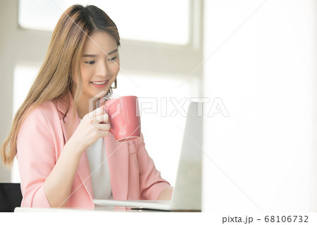 きれいな女性会社員がオフィスでコーヒーを飲みながらパソコンで仕事する 68106732