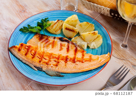 Fried trout fillet with baked potatoes on blue plate 68112187