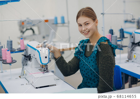 Young beautiful seamstress sews on sewing machine in factory Young beautiful seamstress sews on sewing machine in factory 68114655