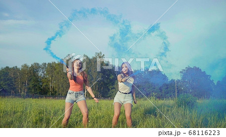 Two happy girls spray blue smoke and make a heart shape out of it. Two happy girls spray blue smoke and make a heart shape out of it. 68116223