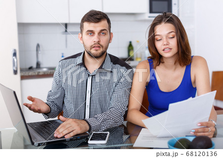Serious young man and woman with financial documents near laptop Serious young man and woman with financial documents near laptop 68120136