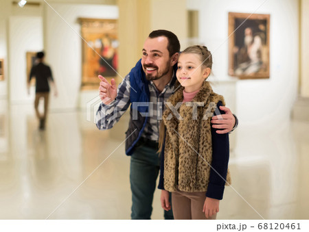 Father and daughter looking at paintings in halls of museum 68120461