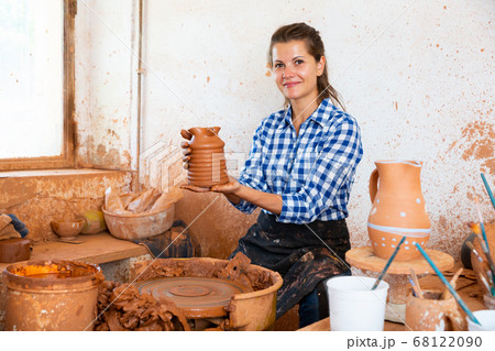 Female artisan in ceramics workshop with pottery wheel and various clay vessels 68122090