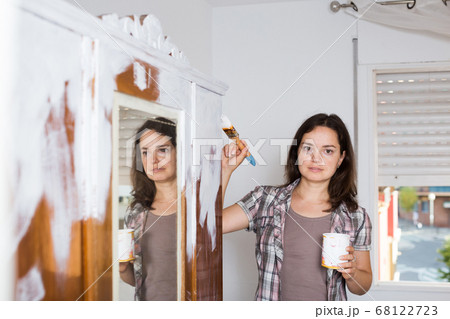 Creative woman is decorating old wardrobe with white paint Creative woman is decorating old wardrobe with white paint 68122723
