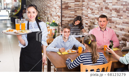 Young smiling wairtess is ready to serve salad and juice to young visitors Young smiling wairtess is ready to serve salad and juice to young visitors 68123279