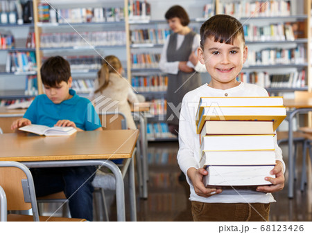 Smiling boy standing with pile of books 68123426